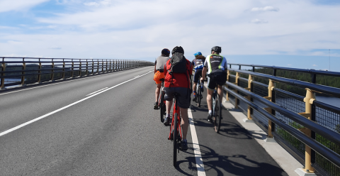 Neljä pyöräilijää ajaa sillalla.